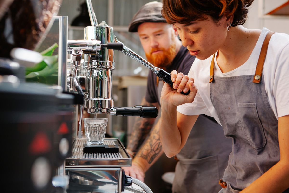 A barista concentrating on making coffee while a colleague looks on